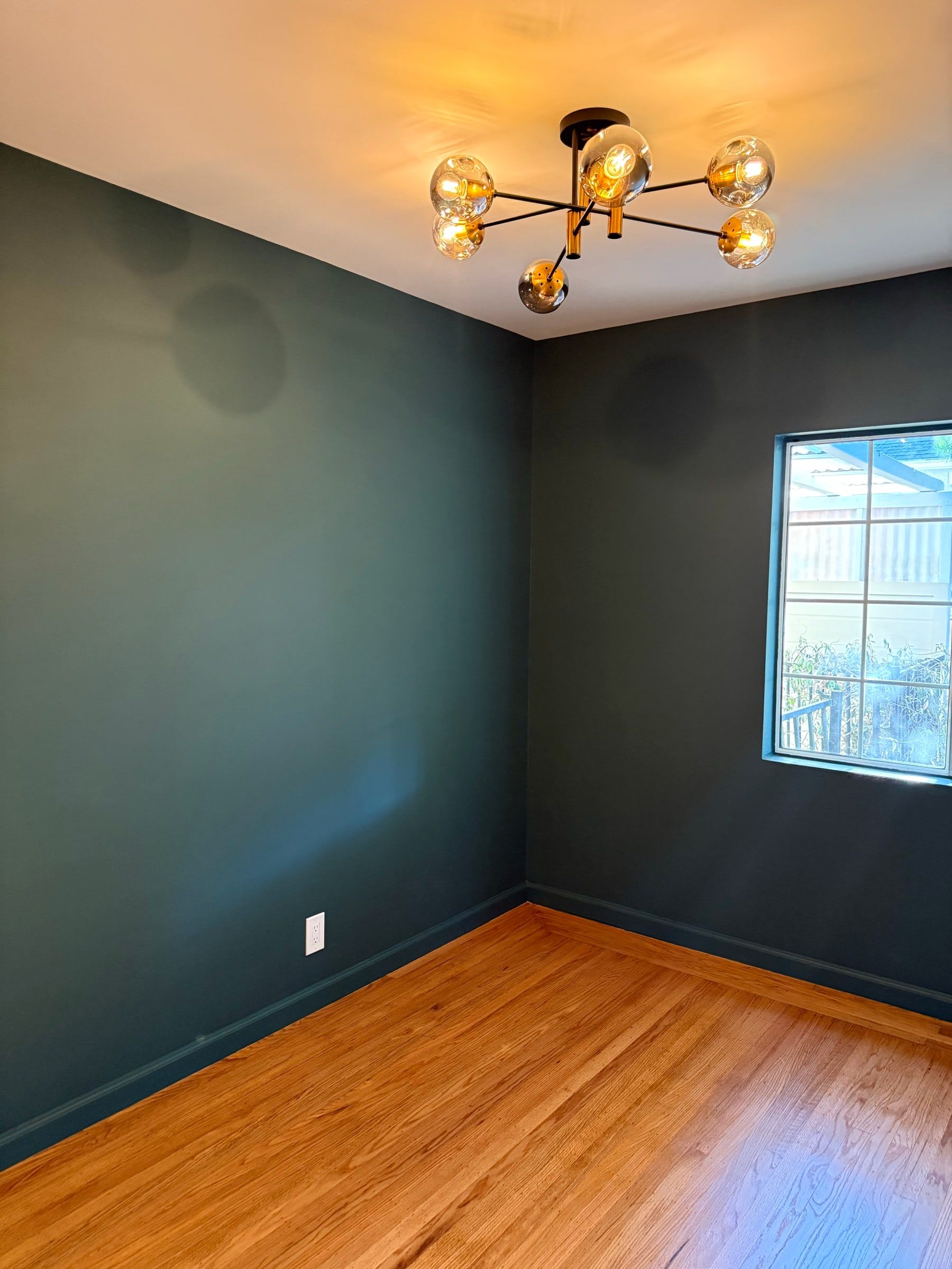 Empty room with dark green walls and polished wood floor after post-construction cleaning