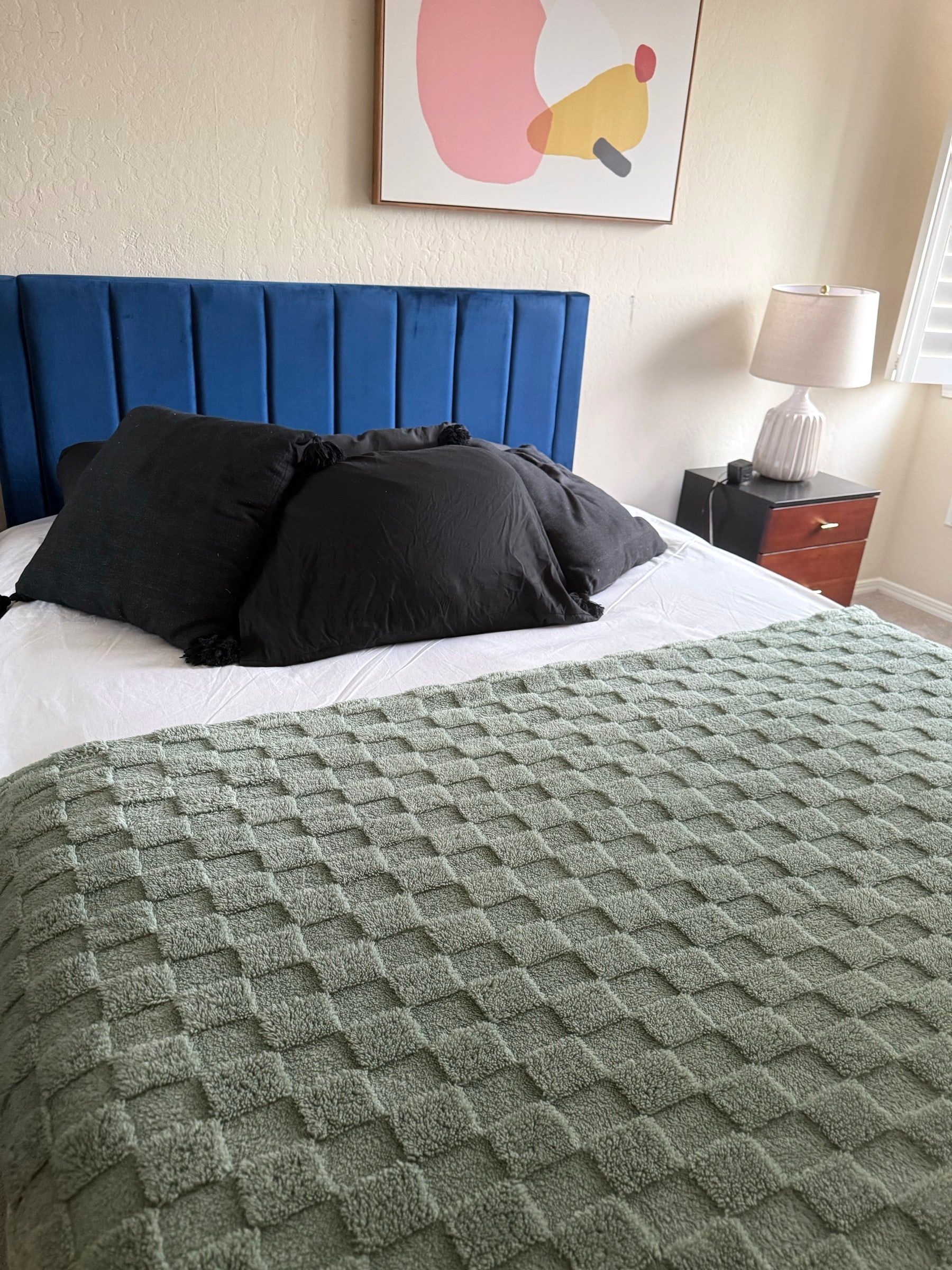 Bedroom with a made bed, green knit blanket and blue velvet headboard